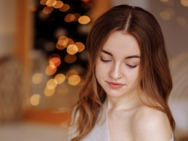 young beautiful woman in a knitted sweater and skirt sits on a bed against the backdrop of a christmax interior