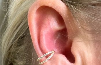 Close-up of a person's ear with a double-layered gold ear cuff adorned with small crystals on the cartilage.