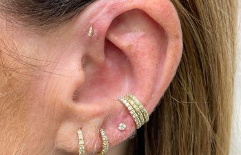 A close-up of a person's ear with multiple gold and diamond hoop earrings and one small diamond stud in various piercings.
