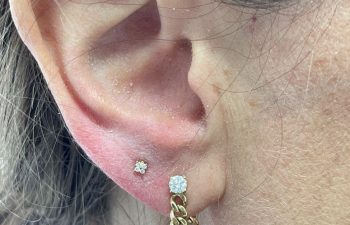 Close-up of an ear with two piercings: one with a small diamond stud and the other with a larger diamond stud attached to a gold chain earring.