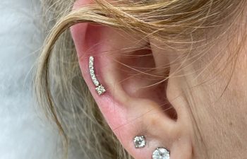 A close-up of an ear with three diamond stud earrings in the lobe and one curved diamond earring in the upper cartilage.