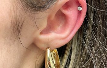 Close-up of a person's ear with a small stud earring in the cartilage and a chunky gold hoop earring in the earlobe.
