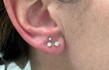 Close-up of a person's ear with three lobe piercings, each adorned with a different sized round diamond stud earring.
