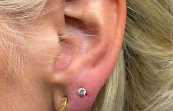 Close-up of a person's ear with a gold hoop earring and a small diamond stud earring in the earlobe.