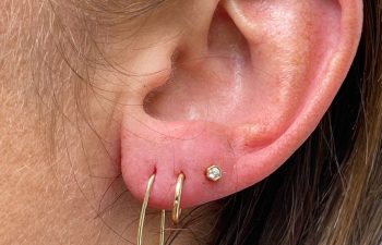 A close-up of a person's ear wearing three earrings: two small gold hoops and one small stud.