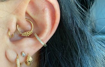Close-up of an ear with multiple gold and silver earrings, including hoops, studs, and a spike-shaped dangle.