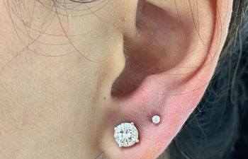 Close-up of an ear with two piercings: one with a large round diamond stud and another with a small round diamond stud placed above it.