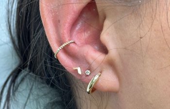 Close-up of a person's ear with multiple gold and diamond earrings, including a hoop, a stud, a curved bar, and a small triangle.