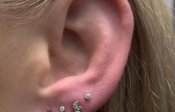 A close-up of an ear with five piercings, featuring small diamond studs, a curved row of three stones, and a thin hoop earring along the outer edge.