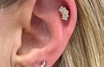 Close-up of a person's ear with three piercings, each adorned with a different style of gold and diamond earring.