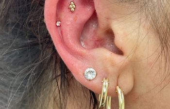 Close-up of a person's ear with four piercings: two gold hoops in the lobe, a diamond stud above them, and two small studs in the inner cartilage.