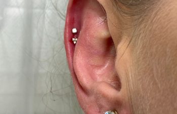 Close-up of a person's ear with three piercings: two small studs in the upper cartilage and one larger stud in the earlobe.