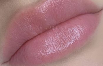 Close-up of natural, full lips with a light pink tint, showing smooth skin texture and a subtle shine.