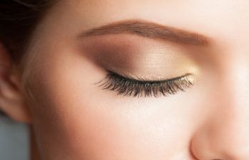 A close-up of a woman's closed eye with long eyelashes and brown and gold eyeshadow.