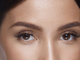 Close-up of a woman's face focused on her eyes and eyebrows, showing smooth skin, neatly shaped brows, and long eyelashes.