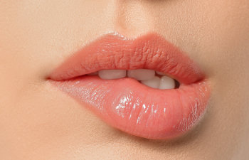 Close-up of a person’s lips with a light pink gloss, upper teeth slightly visible as the lower lip is gently bitten.